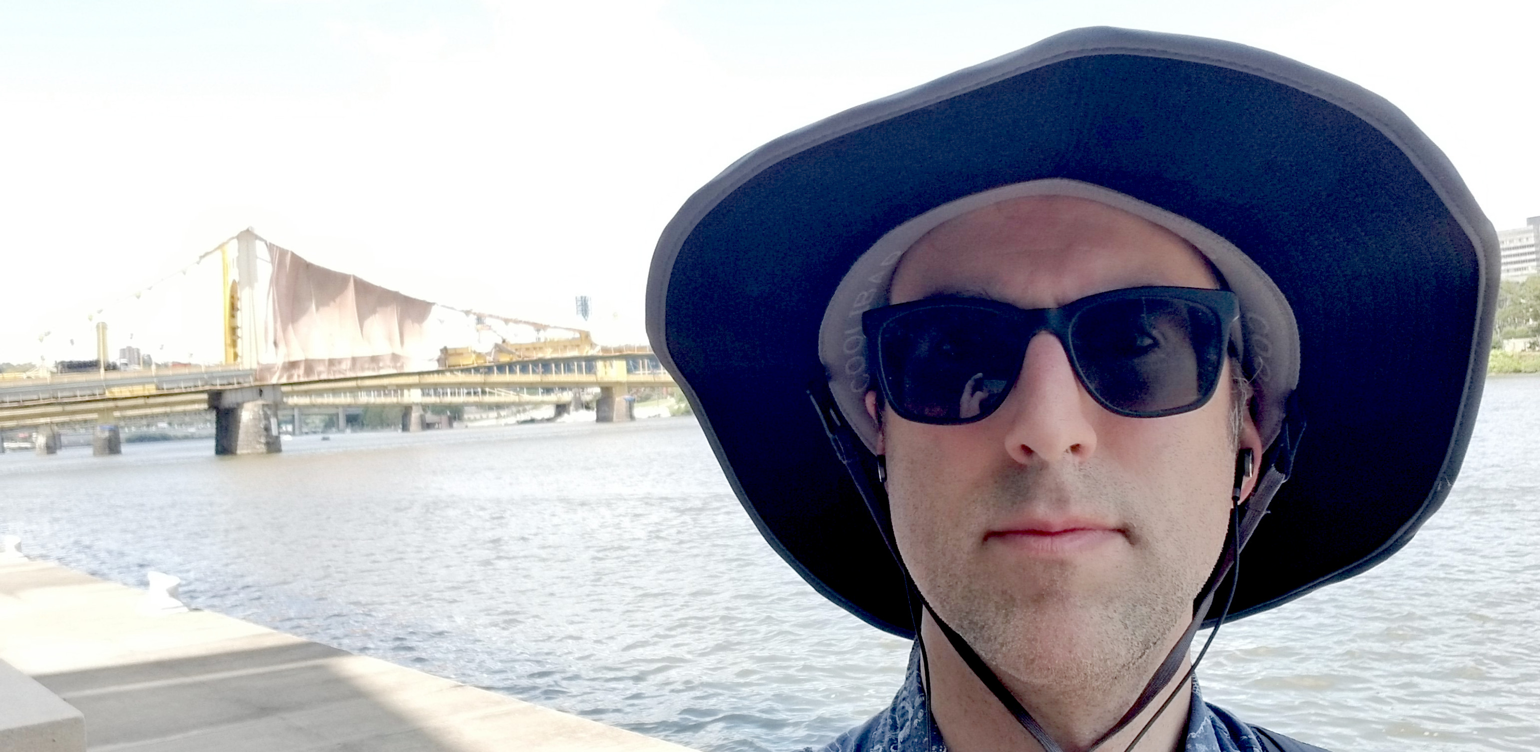 Me on the waterfront in a big hat in front of a bridge